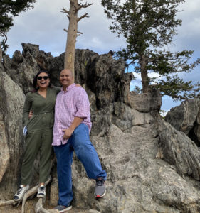 A couple smiles next to a rock formation on a Colorado hiking trail