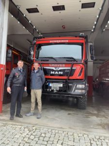 Two men pose in front of a large red fire truck
