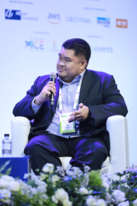 Pasamon Pechrasuwan sits in a chair on a stage, holding a microphone