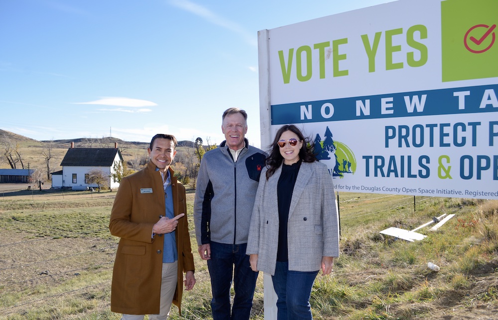 Three people stand next to a sign promoting an open space election