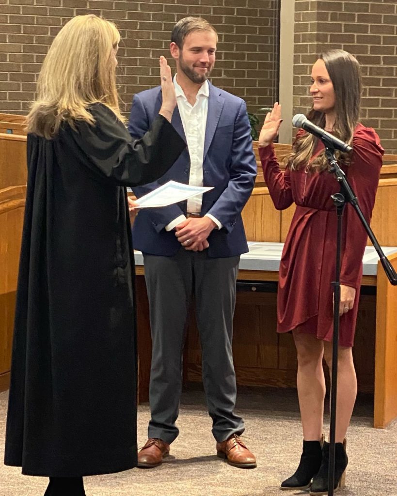 Lisa Smith being sworn in as a Arvada City Council Member with a judge leading the oath and Smith's husband looking on. 