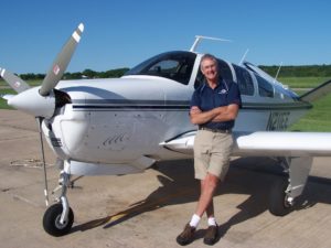 Bob Kinney leans against the wing of a single-prop airplane