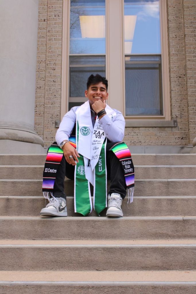 Mario Garcia in his graduation regalia sitting on the steps of a CSU building.