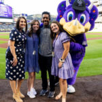 Katie George standing with coworkers and the Colorado Rockies' mascot, Dinger, on Coors Field.
