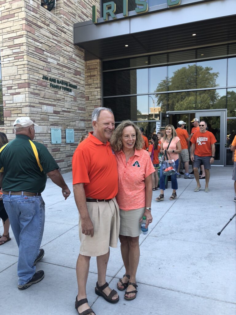 Marc Reck and his wife pose for a photo in front the Iris and Michael Smith Alumni Center 