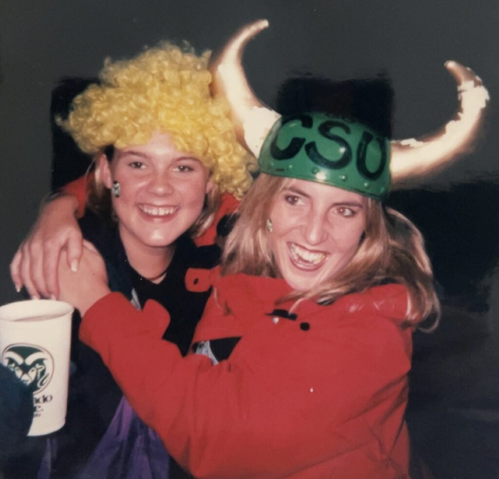 Kristi Pohly during her time as a CSU student supporting the Rams while wearing a viking-style horned helmet standing next to a friend in a yellow wig 