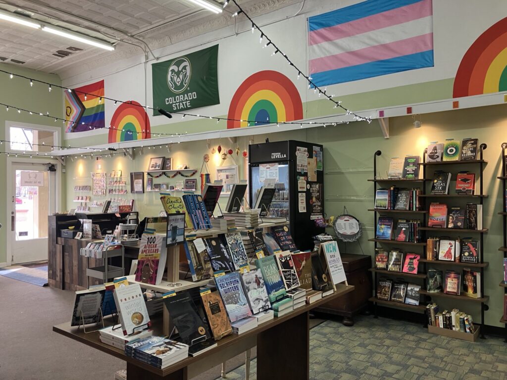 An interior view of Bookstore On The Square showing books on display and an assortment of flags, including an LGBTQ and a CSU flag. 