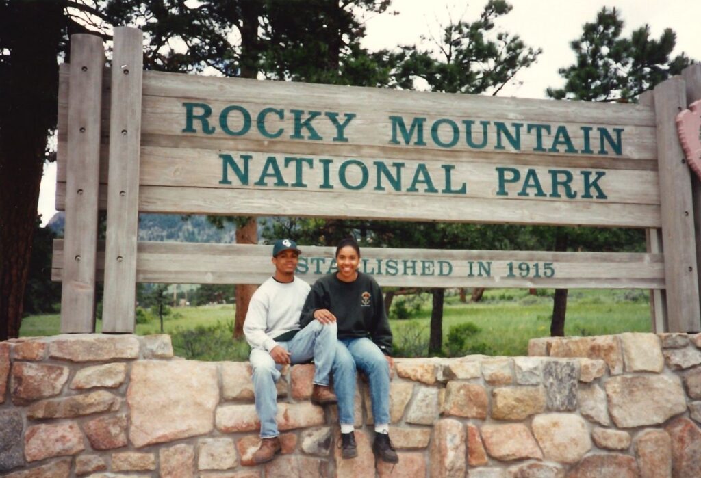 Zenarae and Ronald Antoine sitting in front of the Rocky Mountain National Park entrance sign. 