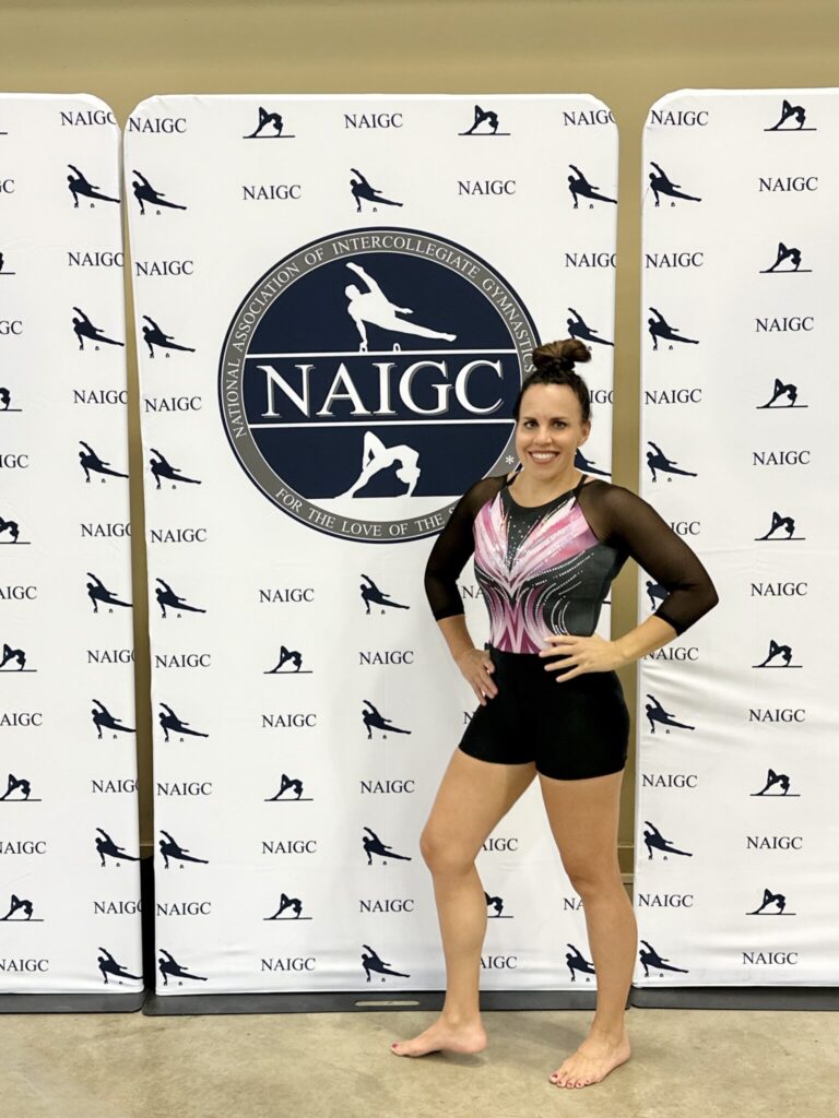 Fuller standing in front of a National Association of Intercollegiate Gymnastics Club sign. 