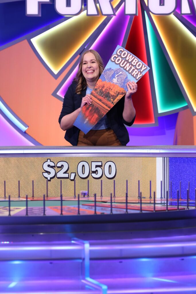 Marissa Rogers holding a prize panel in front of the wheel on wheel of fortune. 